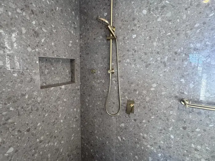 Finished shower after a bathroom renovation plumbing fit-off: terrazzo tiles and brushed gold rail shower