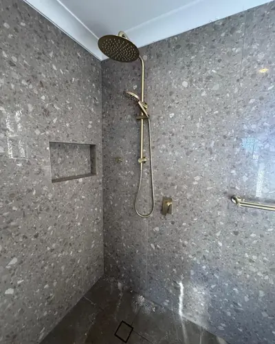 Finished shower after a bathroom renovation plumbing fit-off: terrazzo tiles and brushed gold rail shower