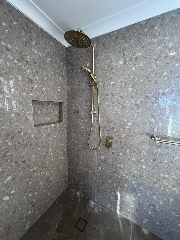 Finished shower after a bathroom renovation plumbing fit-off: terrazzo tiles and brushed gold rail shower