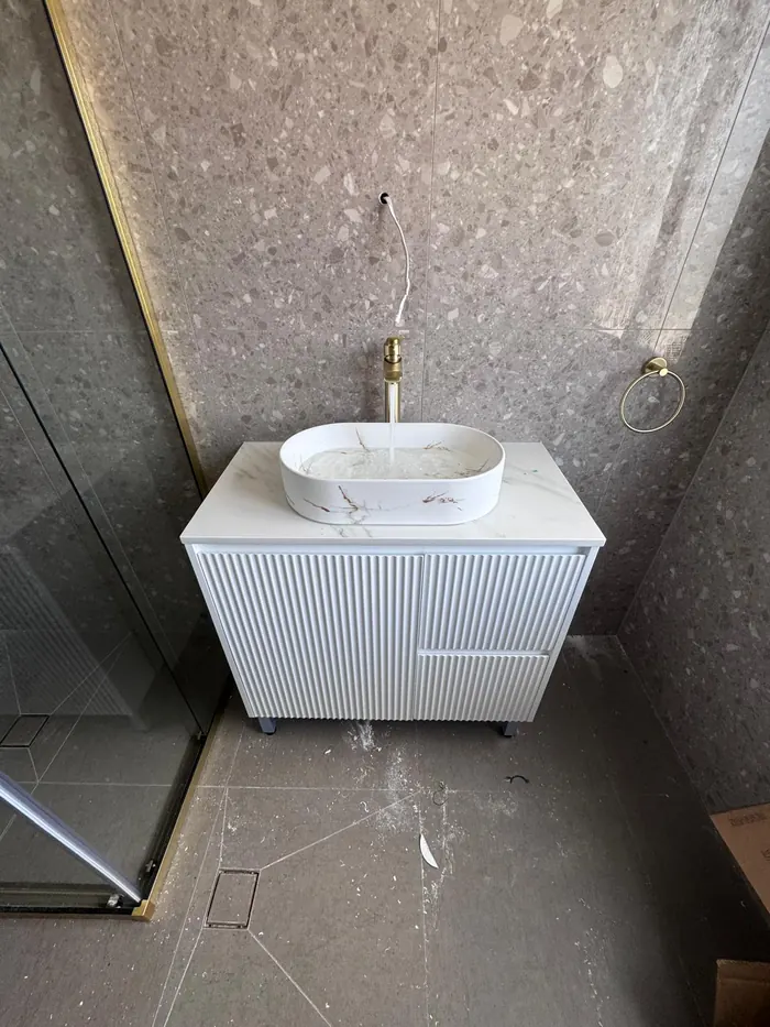 Basin and brushed gold mixer installed on a fluted vanity, water running
