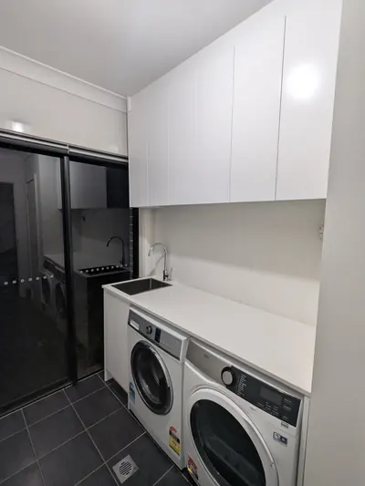 Edmondson Park laundry after: stone benchtop with an inset sink and gooseneck mixer, washer and dryer under the bench, overhead cupboards