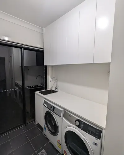 Edmondson Park laundry after: stone benchtop with an inset sink and gooseneck mixer, washer and dryer under the bench, overhead cupboards