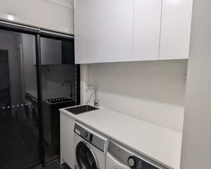 Edmondson Park laundry after: stone benchtop with an inset sink and gooseneck mixer, washer and dryer under the bench, overhead cupboards
