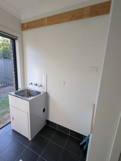 Edmondson Park laundry before: the original builder's tub and wall-mounted taps on a small tiled splashback