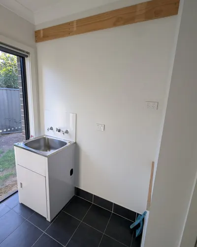 Edmondson Park laundry before: the original builder's tub and wall-mounted taps on a small tiled splashback