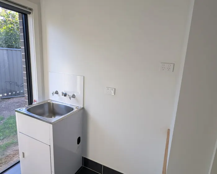Edmondson Park laundry before: the original builder's tub and wall-mounted taps on a small tiled splashback