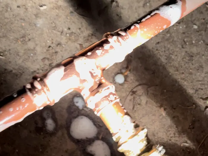 Paul leak-testing a new copper gas tee with soapy water under a house