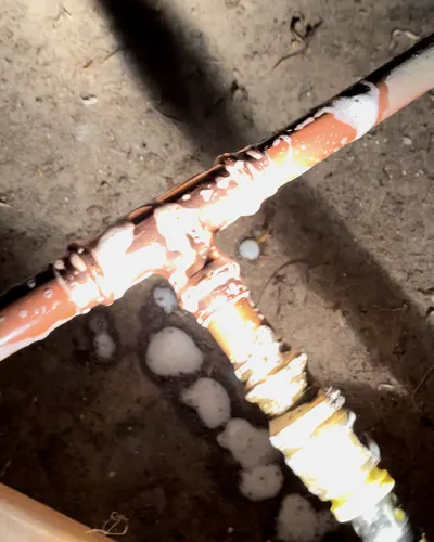 Soapy water leak test on a new copper gas tee under a house