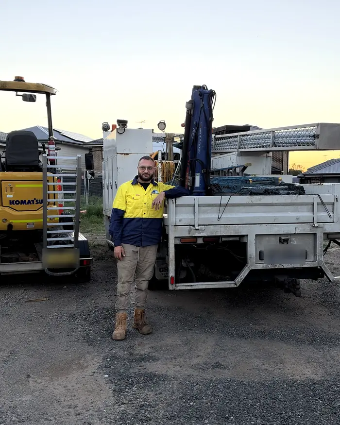 Paul, owner of Monarch Civil & Plumbing, standing between the Komatsu PC18 excavator on its trailer and the crane truck