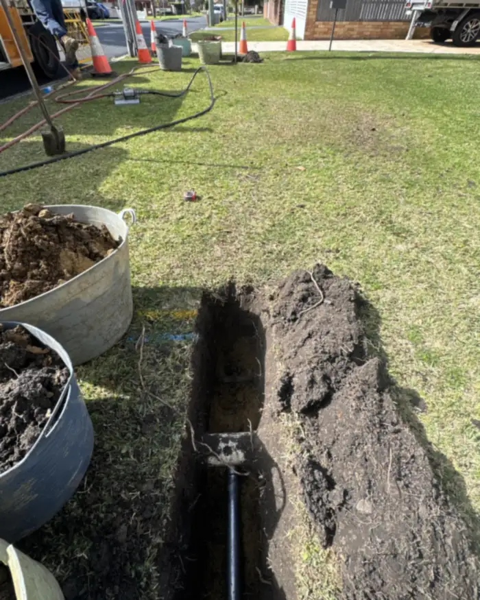 Trenchless bore under way from a small launch pit in the front yard: air hoses back to the compressor on the truck, no trench across the lawn